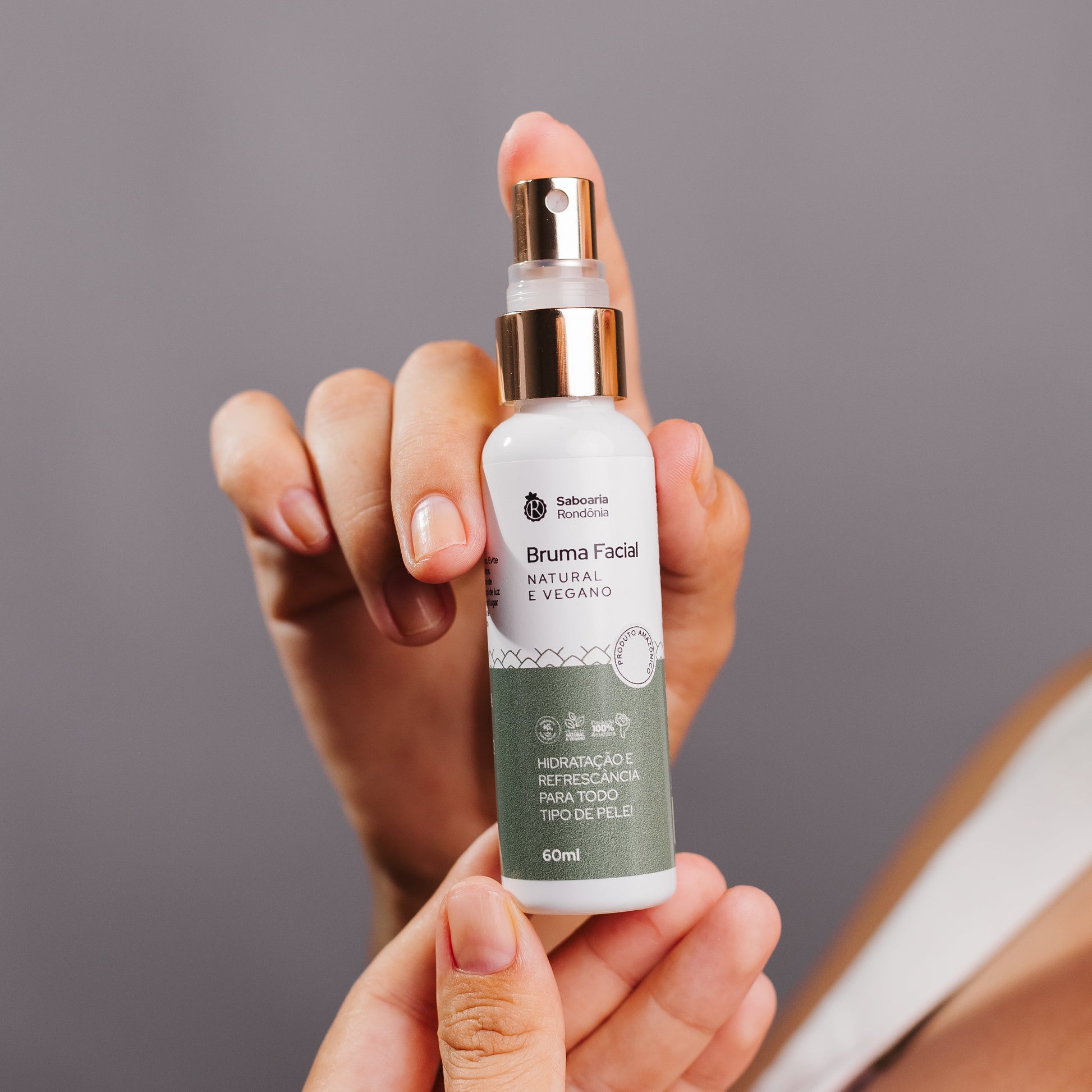 mão segurando o frasco Bruma facial com glicerina, pantenol e óleo essencial de hortelã-pimenta. 
